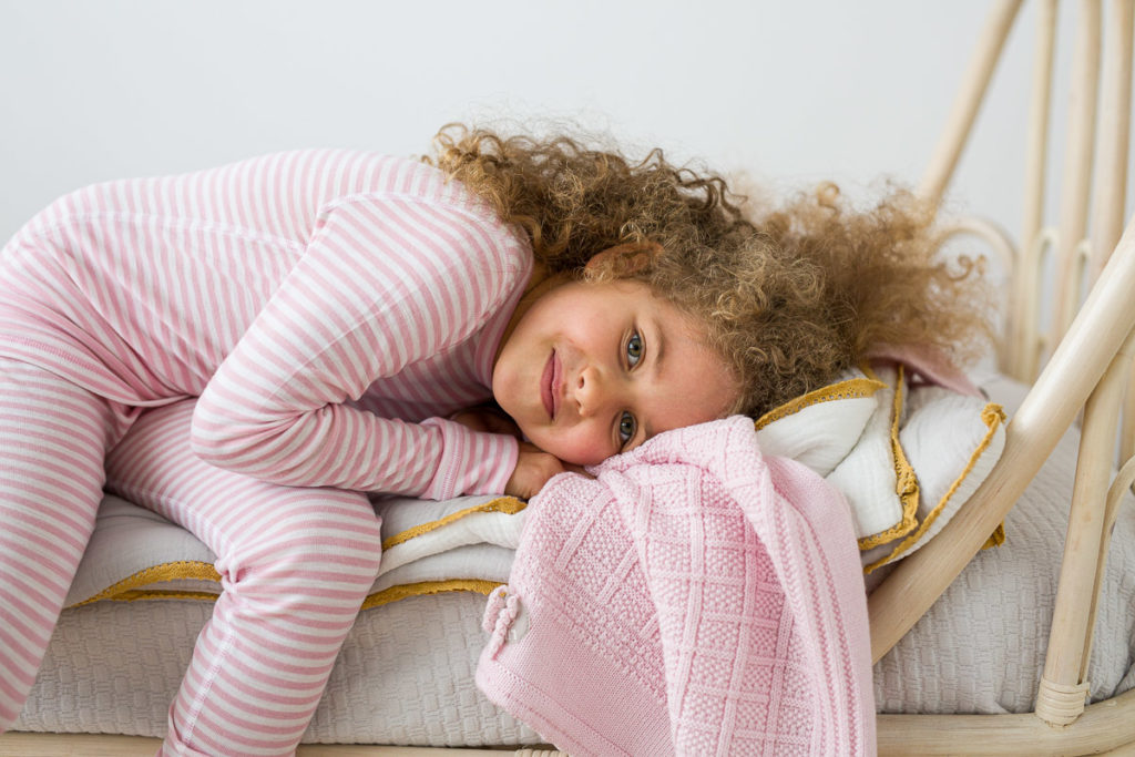 barn liggende på seng med natttøy i merinoull